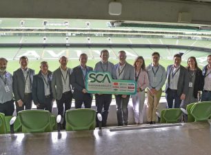 John Paul Construction team members and founding industry partners holding a large green launch sign for the Sustainability Common Assessment (SCA) inside a stadium box overlooking the pitch at the Aviva Stadium, Dublin.
